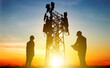 © ฺฺฺBoonterm - Silhouette Engineer worker man and woman working wearing helmets doing field work telecommunication tower holding blueprints controlling installation connectivity equipment maintaining 5G network.