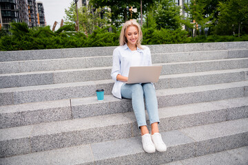 Wall Mural - Full length size photo of smiling young beginner startuper woman texting email using laptop sitting stairs near modern business center