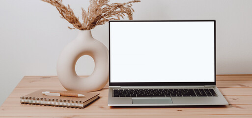 Empty mockup laptop with white screen and notepad, vase at the background, brown tone. Aesthetic laptop background for business, study, work, home office, web site promotion, social media template