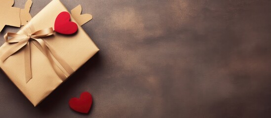 A brown gift box with a bow on top, featuring two hearts cut out of it. Placed on a textured surface with an empty envelope nearby.