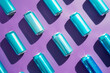 A row of blue cans are arranged in a pattern on a purple background. The cans are all the same color and size, creating a sense of uniformity and order. The image conveys a feeling of organisation.