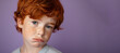 © Nataliia_Trushchenko - A boy with red hair and blue eyes is looking at the camera. He has a scruffy appearance and he is sad. a close up head shot of a red haired young boy pulling a funny face on a plain purple background