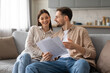 © Prostock-studio - Happy spouses discussing documents on couch at home
