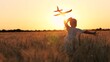 Adorable female kid silhouette running with aircraft toy at cinematic sunset sunrise wheat field back view. Happy little girl child playing pilot game with plane plaything enjoy childhood at dusk