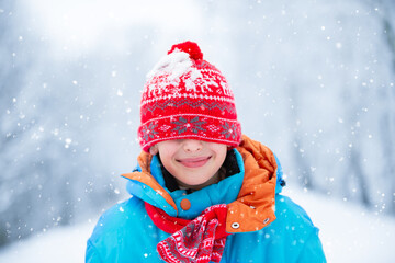 A funny little boy in blue winter clothes walks during a snowfall. The kid is having fun during a snowstorm.