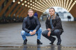 Portrait of two young men sitting on his haunches on background of lights installation main park alley
