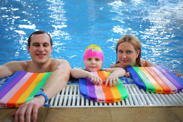 Father, mother and little daughter in a swimming cap in the pool