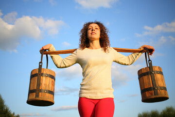 Portrait of a woman with a yoke and wooden pails against the blue sky