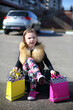 © Pavel Losevsky - Little girl sitting on suitcase with her legs crossed with colored gift bags in middle of road