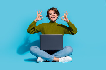 Photo of cheerful glad girl wear stylish clothes sitting floor recommend buy modern device okey sign isolated on cyan color background