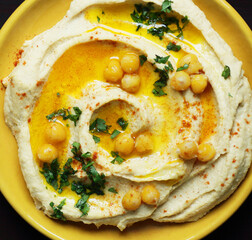 Wall Mural - A plate with hummus with oil, parsley and red pepper along wirh ingredients on wooden board on bright textile, overhead top view, healthy legume food concept