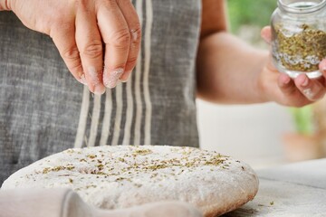 Wall Mural - Bread maker with apron sprinkles spices on top of the bread dough.