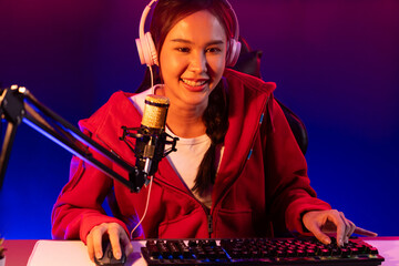 Host channel of smiling beautiful Asian girl streamer playing online game wearing headphone talking with viewers media online recording phone. Esport skilled team players in neon blue room. Stratagem.