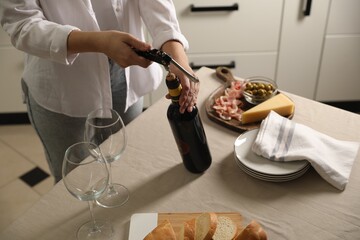 Wall Mural - Woman opening wine bottle with corkscrew at table indoors, closeup