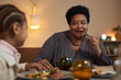 Portrait of African American senior woman enjoying dinner with family sitting at table together and eating food copy space 