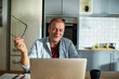 © Marko Geber - Smiling man with glasses using laptop in kitchen