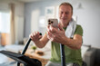 © Marko Geber - Middle aged man using smartphone on home exercise bike