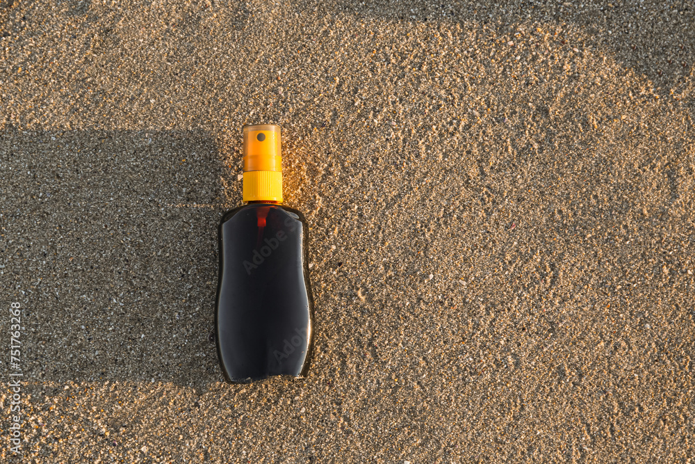 Bottle of sunscreen cream on sand at sea beach