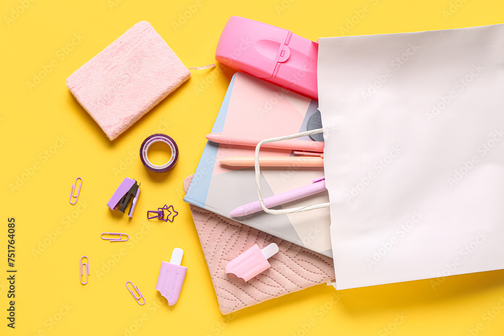 Composition with paper bag with different stationery on yellow background, closeup