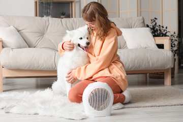 Sticker - Young woman with Samoyed dog warming near electric fan heater at home