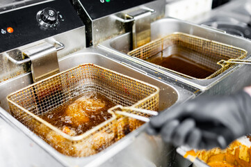 Wall Mural - golden-brown fried chicken wings being lifted from a commercial kitchen fryer. The stainless steel fryer contains several crispy wings. A person’s gloved hand holds the basket handle