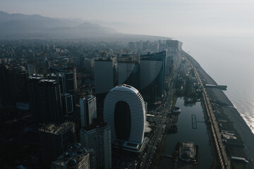 Wall Mural - Aerial view of modern Batumi city skyline against a mountain backdrop, illuminated by the morning sun, reflecting off the buildings and ocean. 