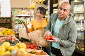 Married couple choosing ripe tomatoes at grocery store