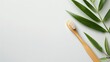 Eco-friendly bamboo toothbrush next to vibrant green leaves on a white surface