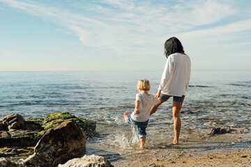 mother and son go into the sea. mother and son test the water with bare feet. mother and son having fun on the seashore. Mum and toddler family time