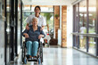 Female nurse compassionately assisting an elderly Caucasian patient in a wheelchair through a retirement home, showcasing professional medical care.

