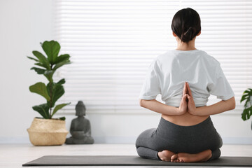 Wall Mural - Girl practicing vajrasana with namaste behind back on mat in yoga studio