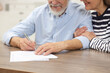 © New Africa - Happy senior couple signing Last Will and Testament at wooden table, closeup