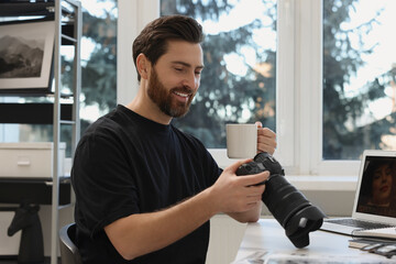 Canvas Print - Professional photographer with digital camera and cup of drink at table in office