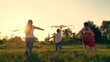 Kite flies in hands of child in summer in park. Kids runs across field at sunset, raising his hands. Mom Boy, girl play with toy kite in park in spring. Children toy plane. Family dreams of traveling