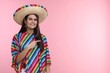 © New Africa - Young woman in Mexican sombrero hat and poncho pointing at something on pink background. Space for text