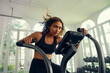 Focused young multiracial woman in sports clothing cycling on exercise bike at the gym