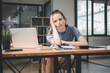 © Satori Studio - A woman takes a thoughtful pause, resting her head on her hand, as she contemplates her work amidst an array of papers and a laptop on her desk in a spacious, contemporary office.