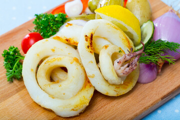 Wall Mural - Cooked tasty squid rings at plate with potatoes and fresh vegetables and herbs