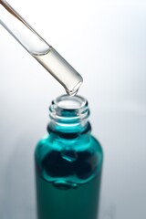 Dripping moisturizing serum from pipette into bottle on light grey background, closeup