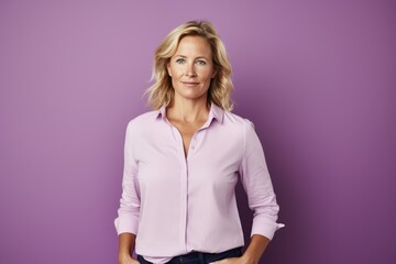 Sticker - Portrait of a beautiful middle aged woman with blonde hair in a pink shirt standing against a purple background