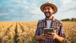 A happy farmer with a straw hat using a tablet in a golden wheat field, signifying modern agriculture.