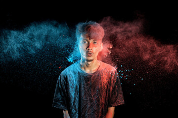 Sticker - Asian man splashed with colorful holi powder and having fun isolated on black background.