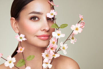 Wall Mural - beautiful young woman with a cherry blossom branch. model with clean fresh skin, close up portrait. 
