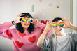 © Johnér - Smiling young LGBTQIA friends covering eyes with rainbow badges against wall