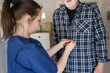 © Johnér - Female caregiver helping while buttoning shirt of elderly man at home