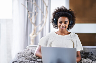 Canvas Print - Laptop, music and smile with afro black woman on sofa in living room of home for social media browsing. Computer, streaming and headphones with happy young person in apartment for weekend comfort