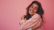 Stunning brunette in casual attire on pink backdrop embracing herself with a joyful and self-assured smile, promoting self-love and self-care.