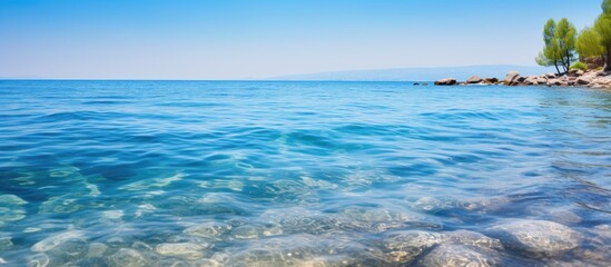 Poster - Tranquil Coastal Scene: Crystal Clear Blue Waters and Sunlit Stones Beneath a Perfect Sky
