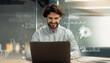 © Prostock-studio - A cheerful bearded man engaging with a laptop in a modern office setting, digital graphs