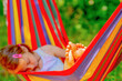 Young beautiful girl sleeping in a hammock with bare feet, relaxing and enjoying a lovely sunny summer day. Green vegetation in background. Happy childhood concept